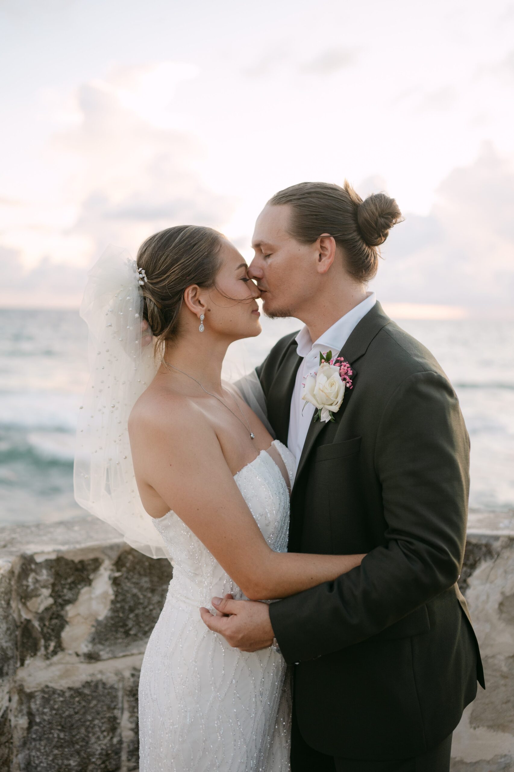 Groom kisses bride's forehead at sunset.