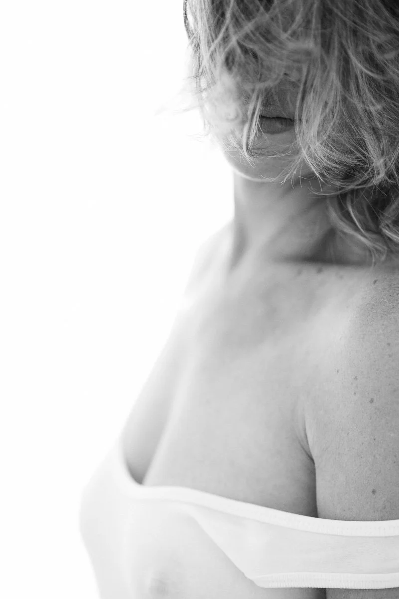 A woman with curly hair partially covering her face, shown in black and white from the shoulders up.