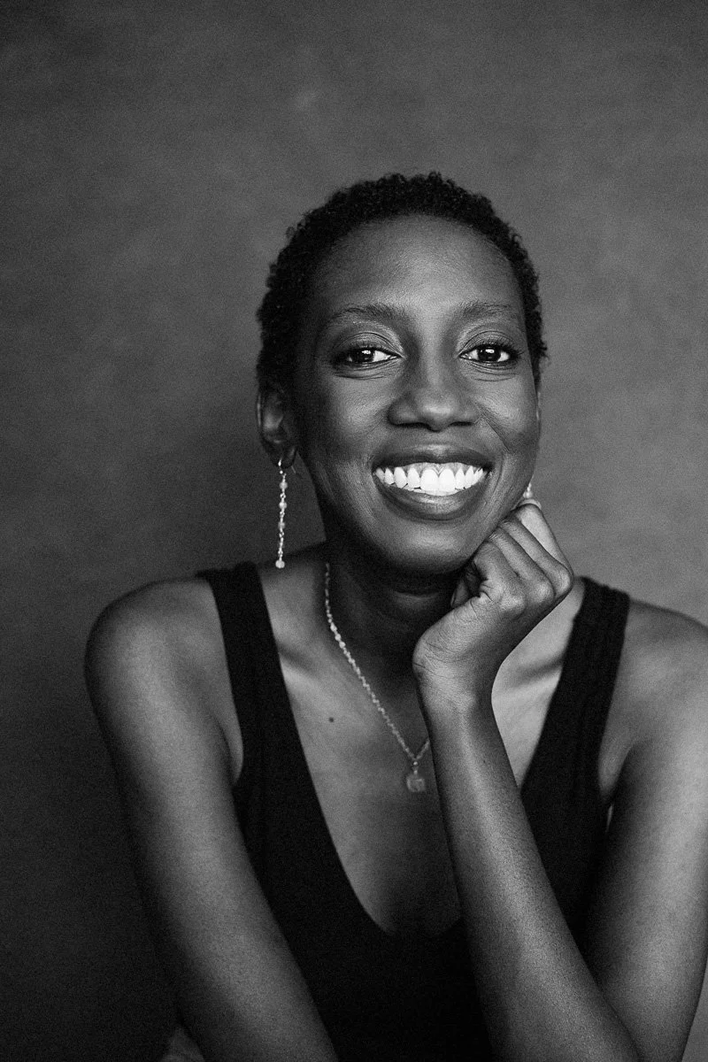 Black and white portrait of a smiling woman with short curly hair, wearing a sleeveless top, earrings, and a necklace.