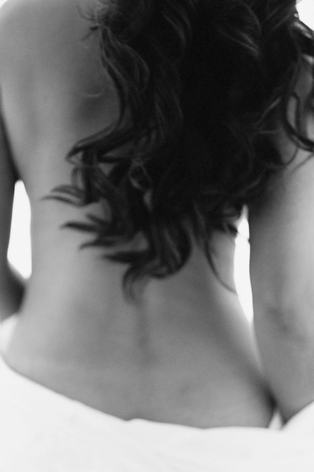 Close-up black and white photo of a woman's back, showing her curly hair and bare shoulders.