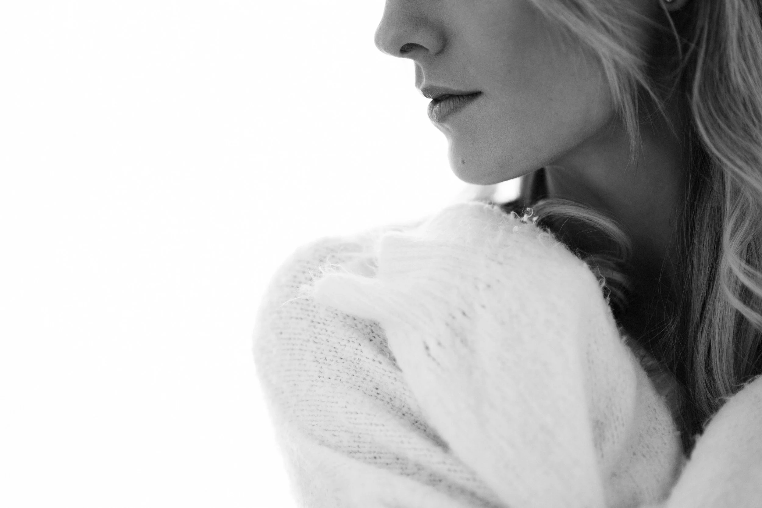 Close-up black and white photo of a woman with long hair, wearing a white sweater, resting her face on her arm.