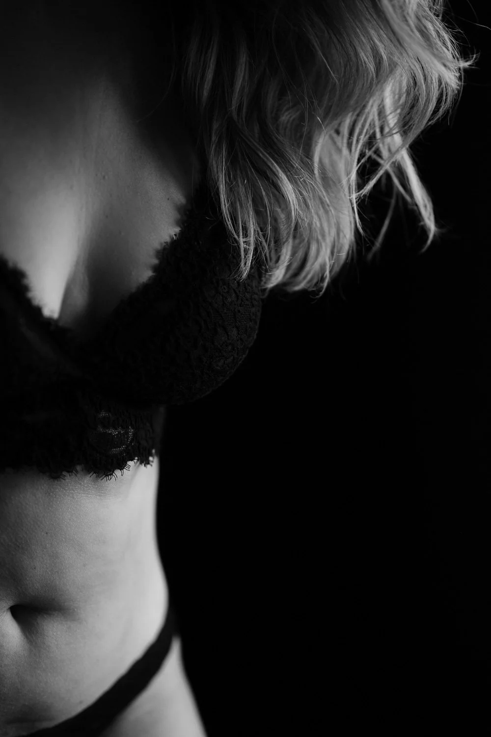 Close-up black and white photo of a woman's shoulder, neck, and part of her face, with her hair covering her face, against a dark background.