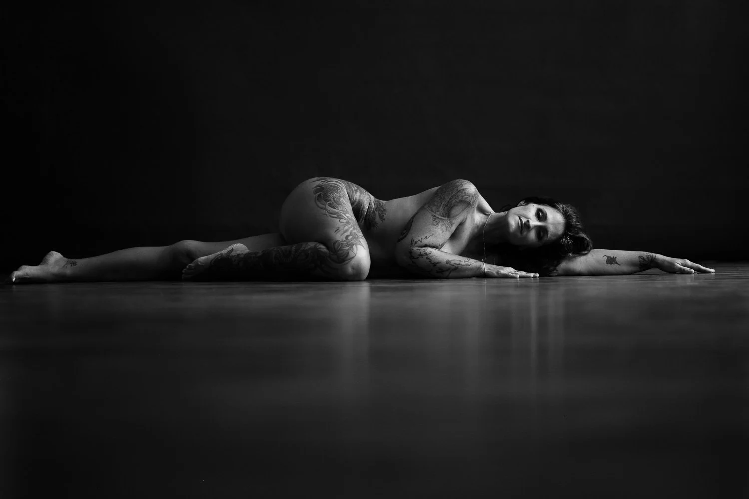 Woman with tattoos lies down in an implied black and white photograph. Photographed by Aniya Emtage Photography in Barbados. Aniya challenges the notion of "embracing" imperfections. 