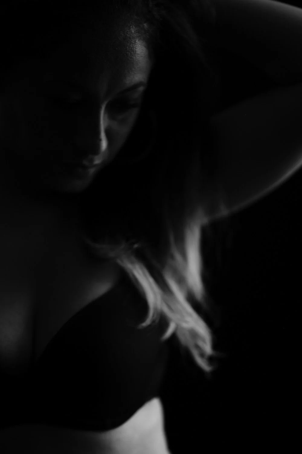 A female figure with long hair and a contemplative expression in low, dramatic lighting, with her face partially shadowed.