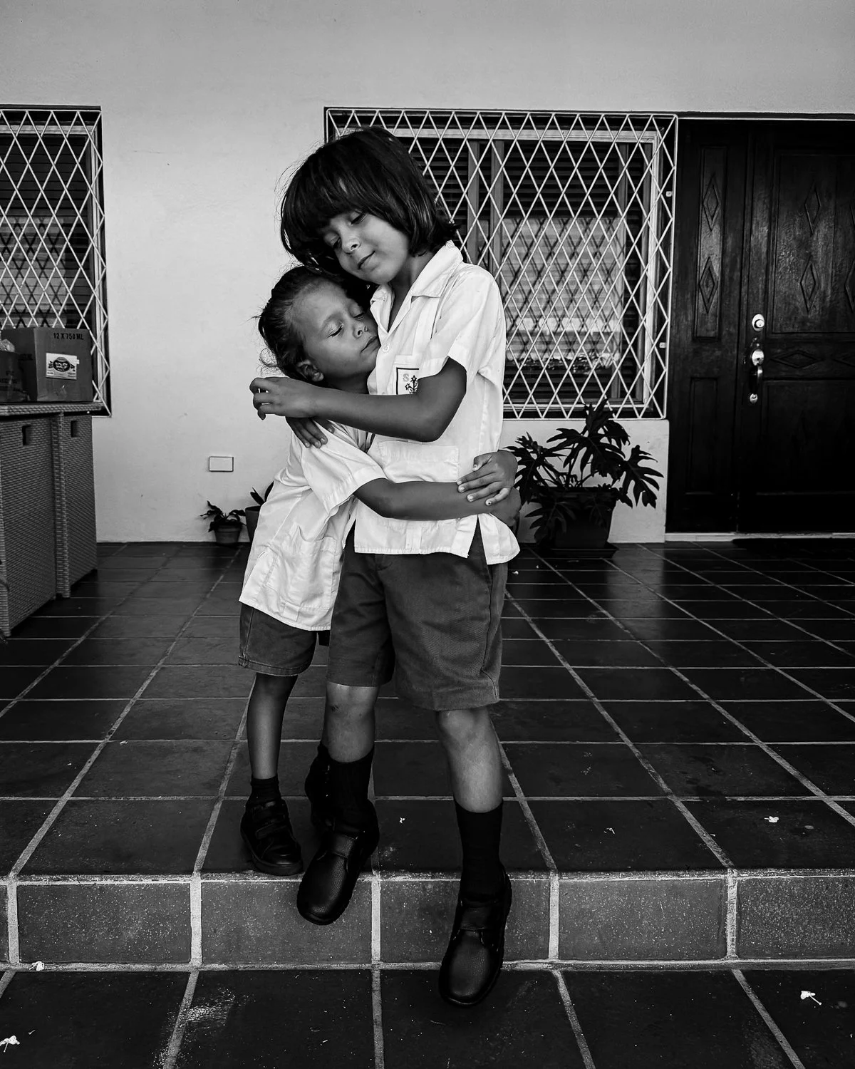 Two children in school uniform sharing an embrace inside a room.
