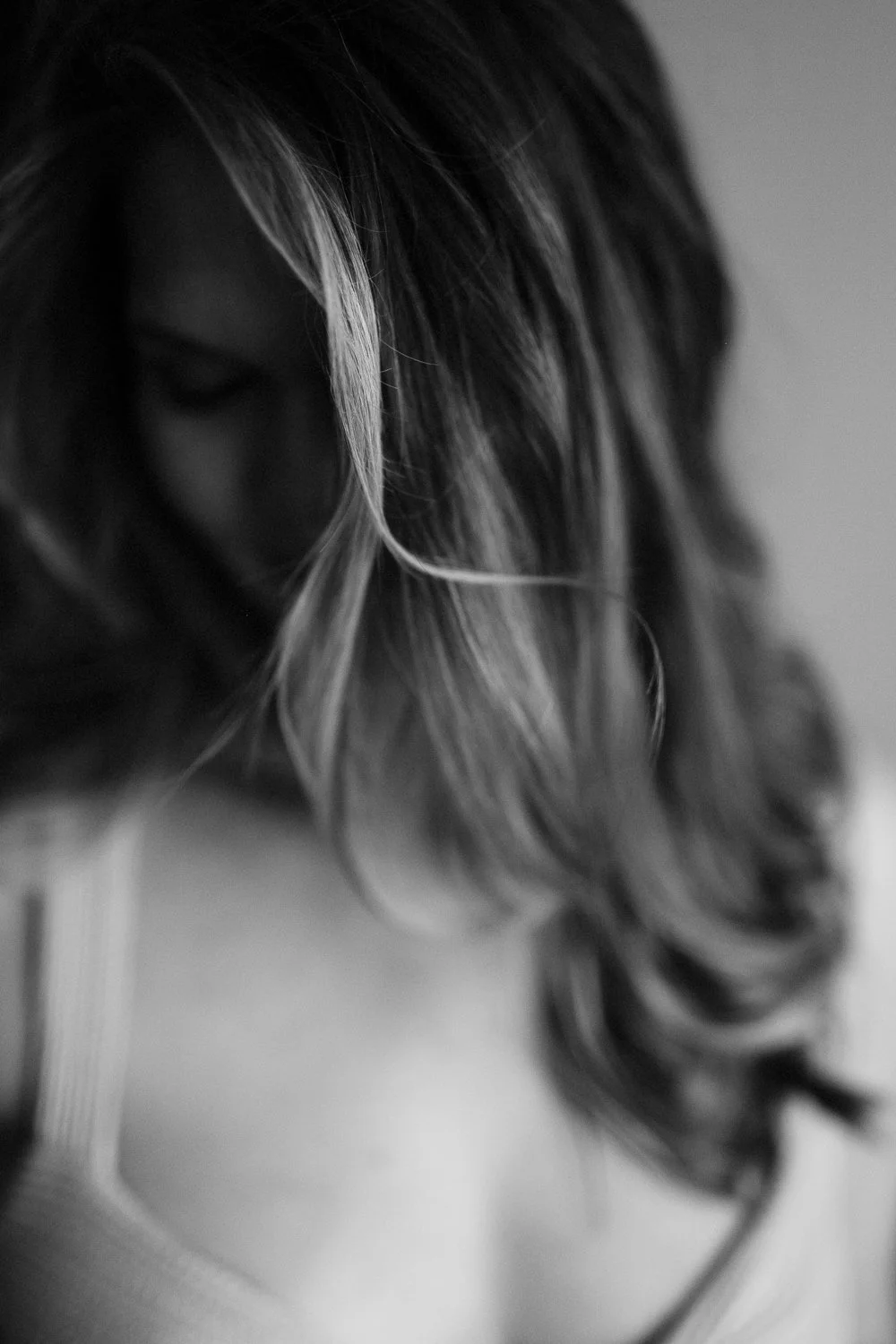 Black and white close-up of a woman's hair, with soft curls and a highlighted streak, partially covering her face.