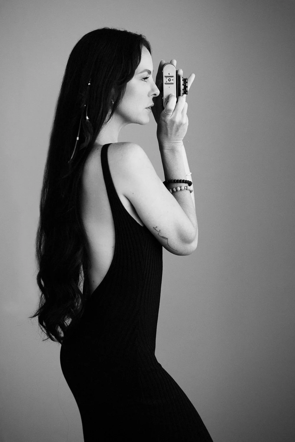 A woman with long hair taking a photo with a camera in black and white.