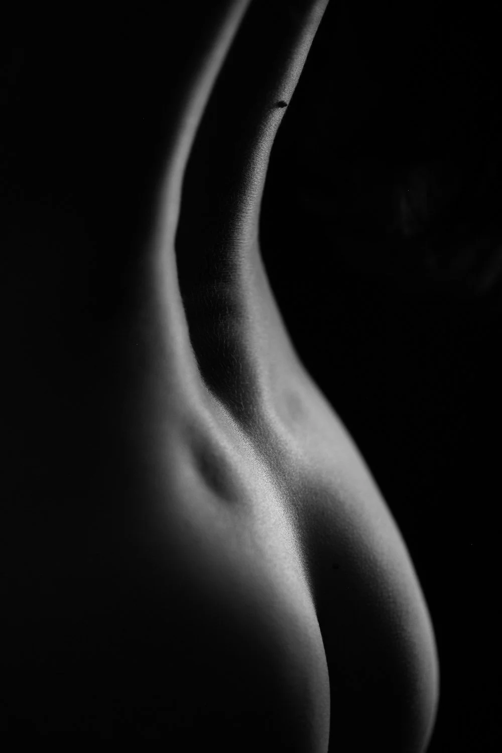 Close-up black and white photo of a human body highlighting the curves of the back and shoulder.