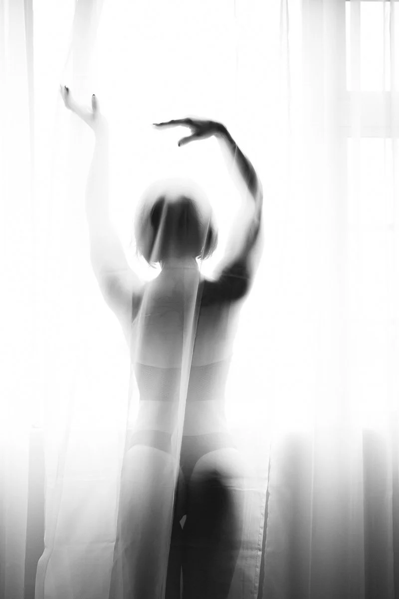 Silhouette of a woman in lingerie standing behind a semi-transparent curtain, with light filtering through.