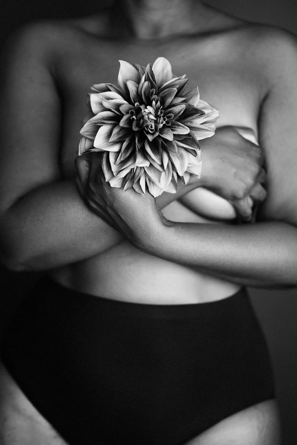 A person holding a large flower in front of their chest, with their arms and torso visible. The image is in black and white.