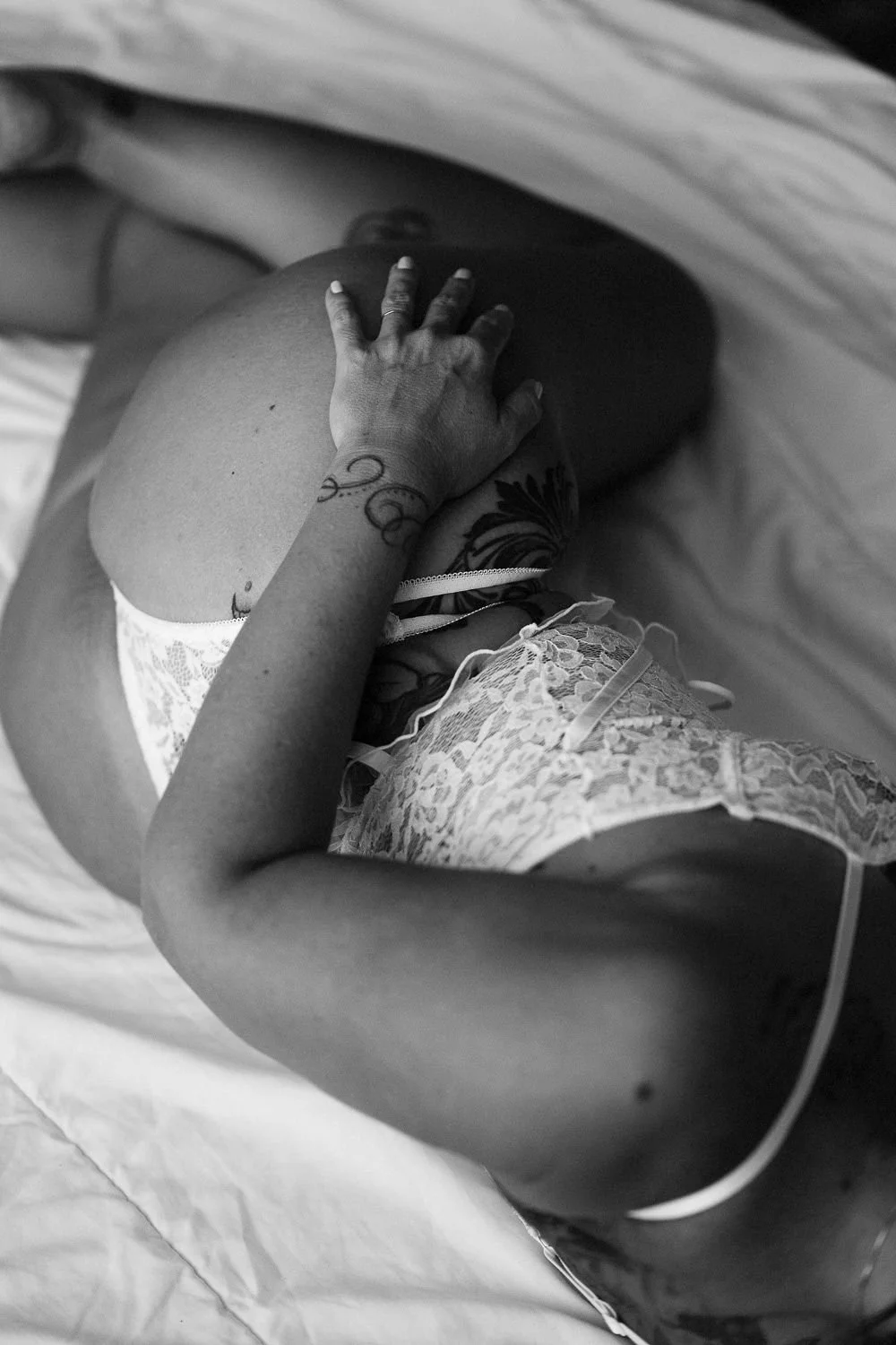 A woman lying on her side on a bed, wearing lacy lingerie, with her hand resting on her pregnant belly.