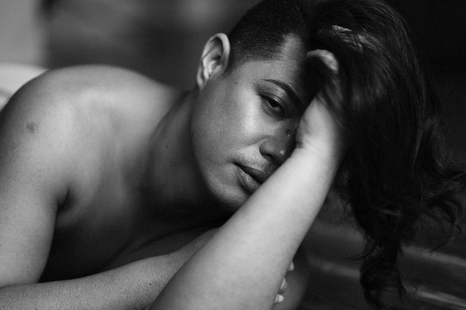 A black and white close-up photo of a woman resting her head on her arm, with her eyes half-closed and long hair flowing.