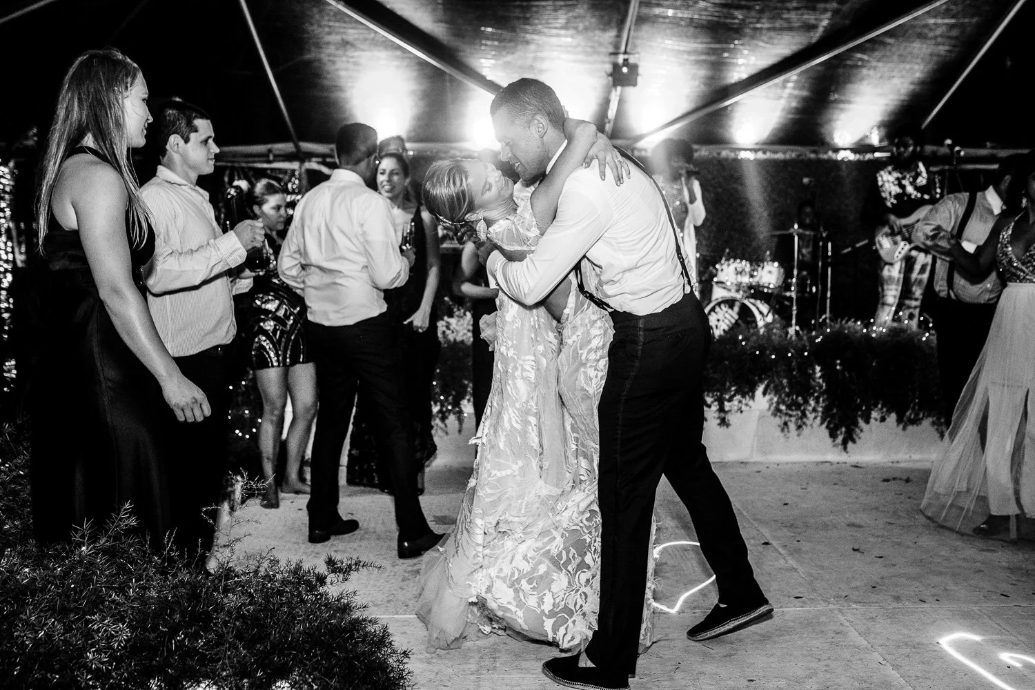 Black and white photo of a wedding reception, with a bride and groom dancing, surrounded by guests.