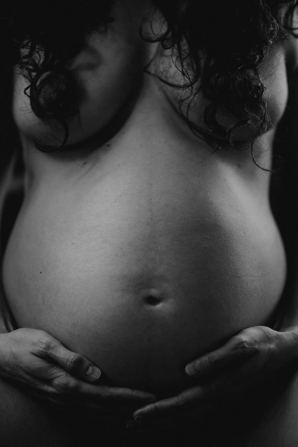 Close-up of a pregnant woman's bare belly with hands gently holding it, black and white photo