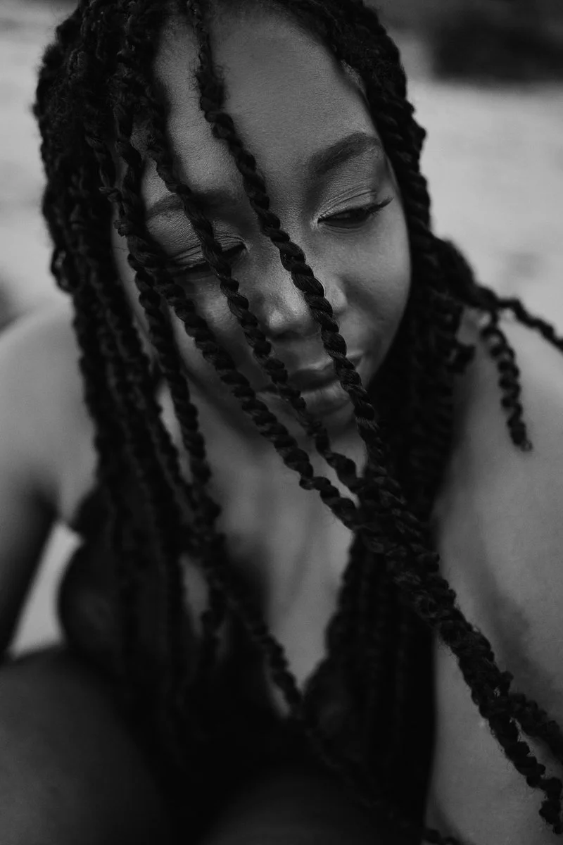 A close-up black and white photo of a woman with long, twisted braids, looking downward with a peaceful expression.