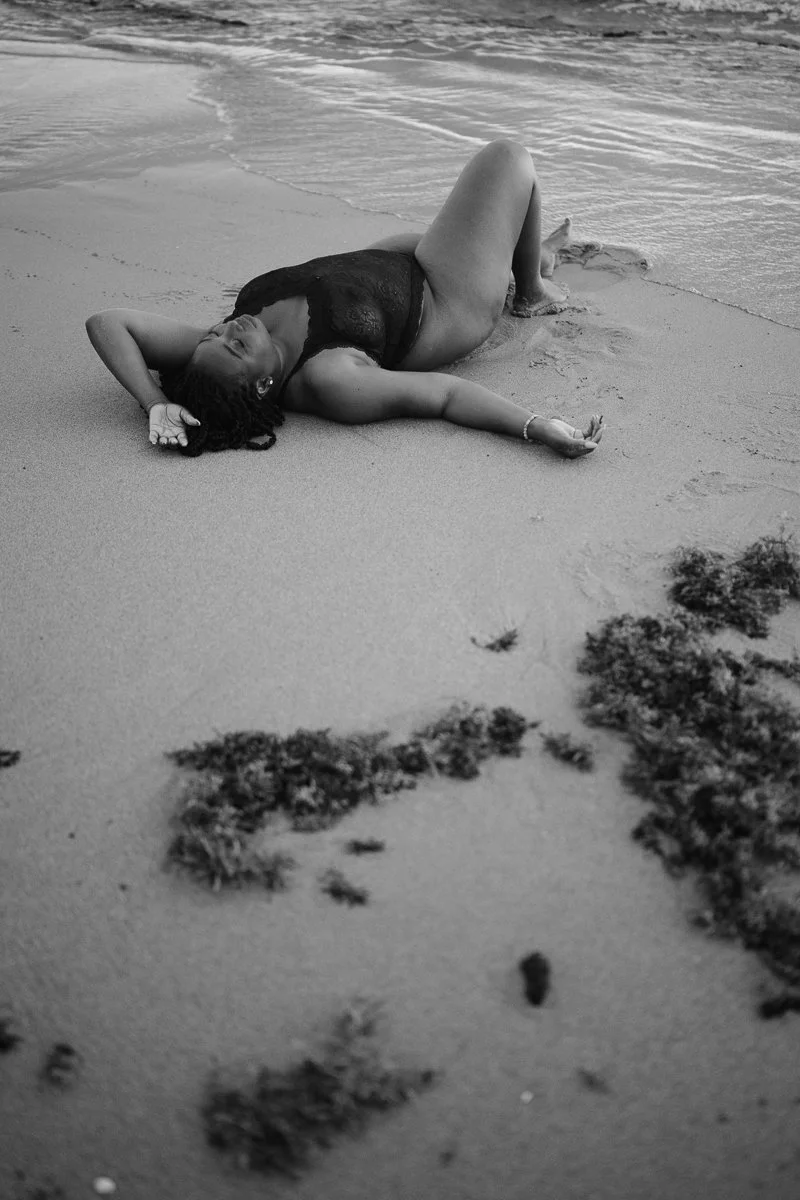 A woman lying on her back on the beach, relaxing near the shoreline in black and white.