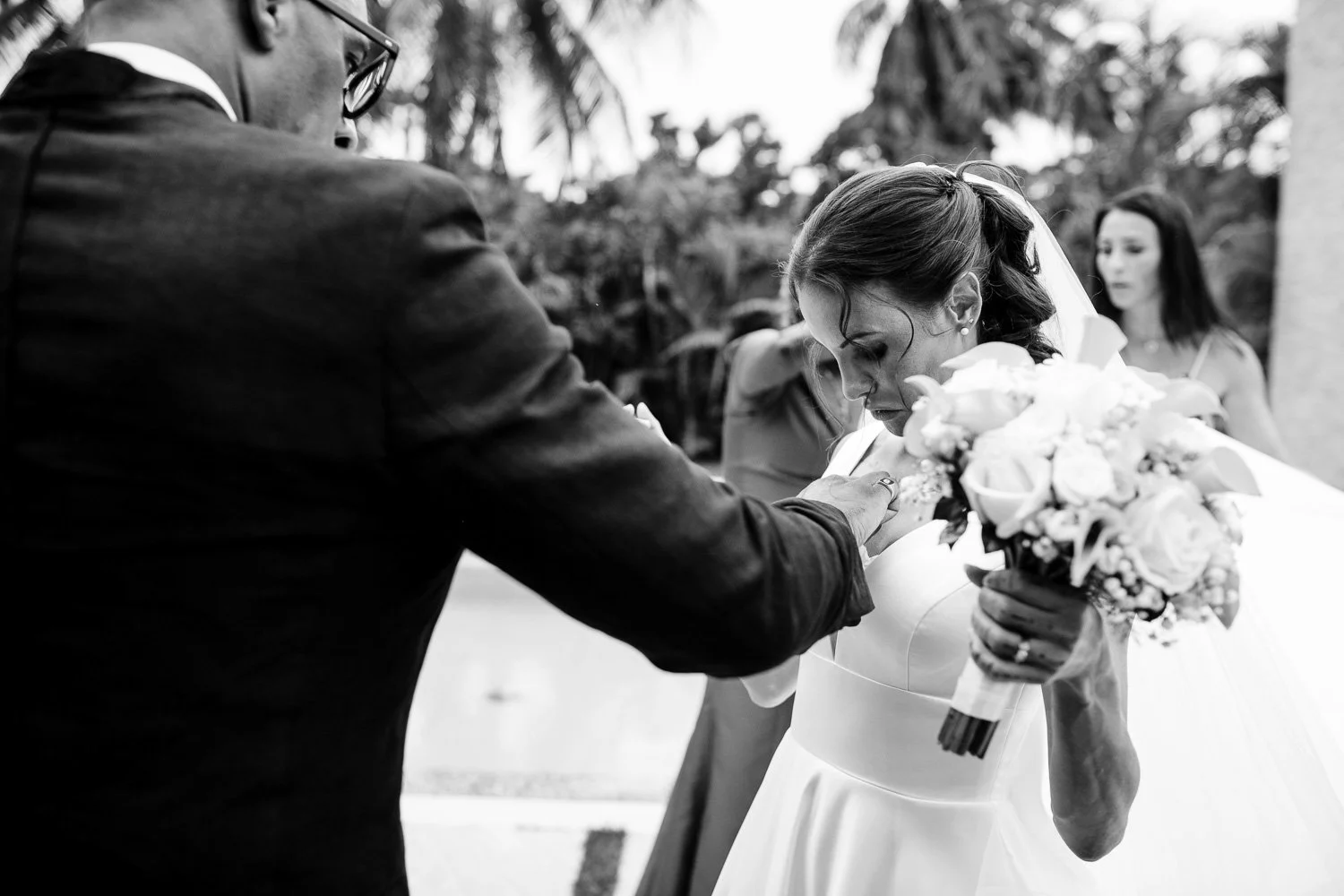 A bride holding a bouquet of flowers is being handed something by a man dressed in a suit during a wedding ceremony.