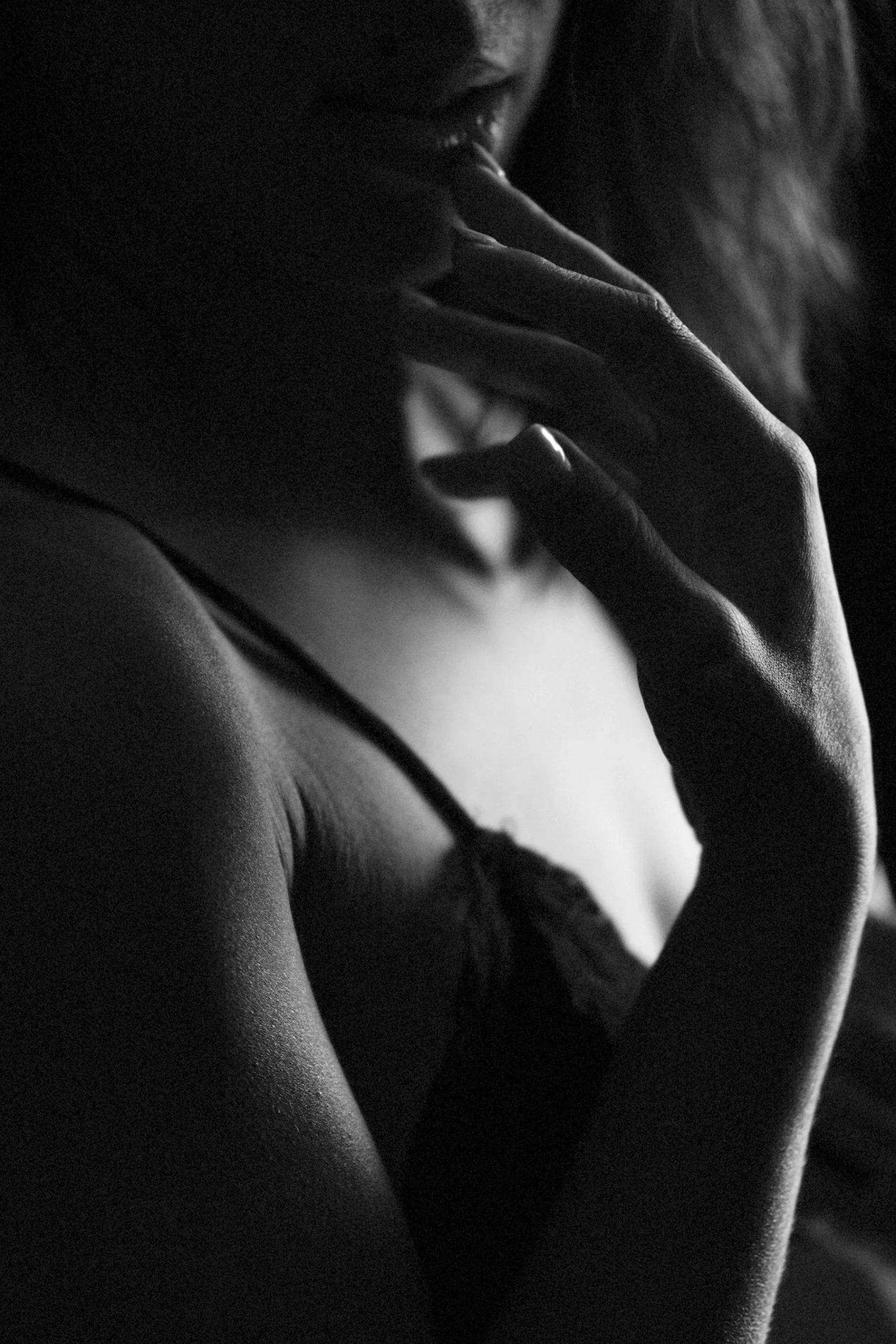 Close-up of a woman touching her lips with her fingers, in a black-and-white photo, with soft lighting highlighting her skin texture.