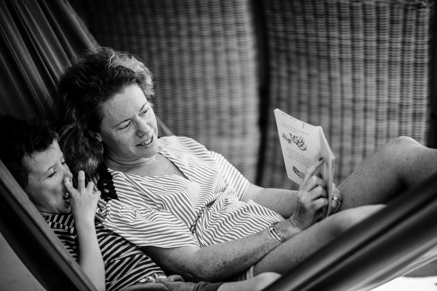 A woman and a young girl relaxing together in a hammock, reading a book and enjoying each other's company.