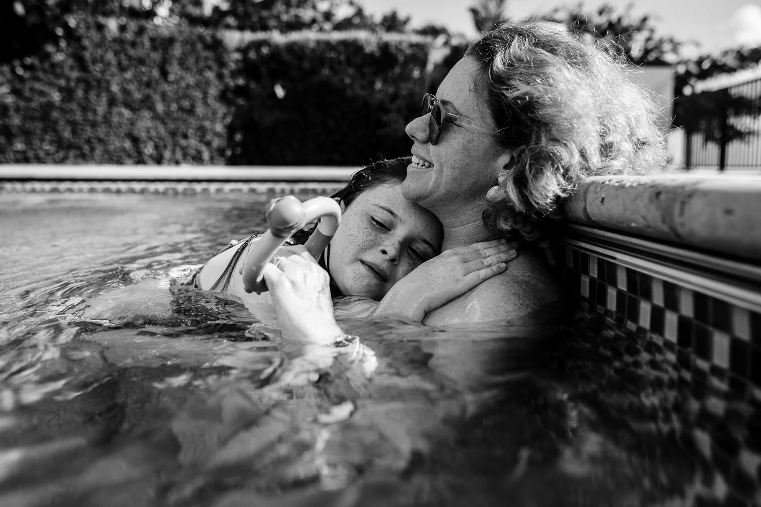 A young girl embracing an older woman in a swimming pool, both smiling and enjoying the moment, in black and white.