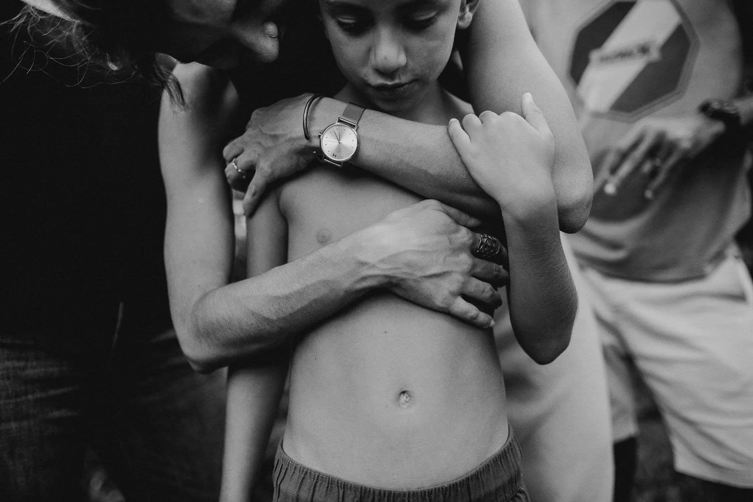 A person with minimal clothing is being held and embraced by multiple hands, with various people surrounding them.