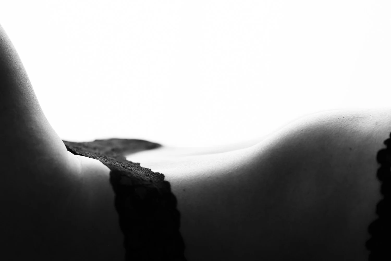 Close-up black-and-white photograph of a person lying on their stomach, focusing on their back, with a lace garment partially visible.
