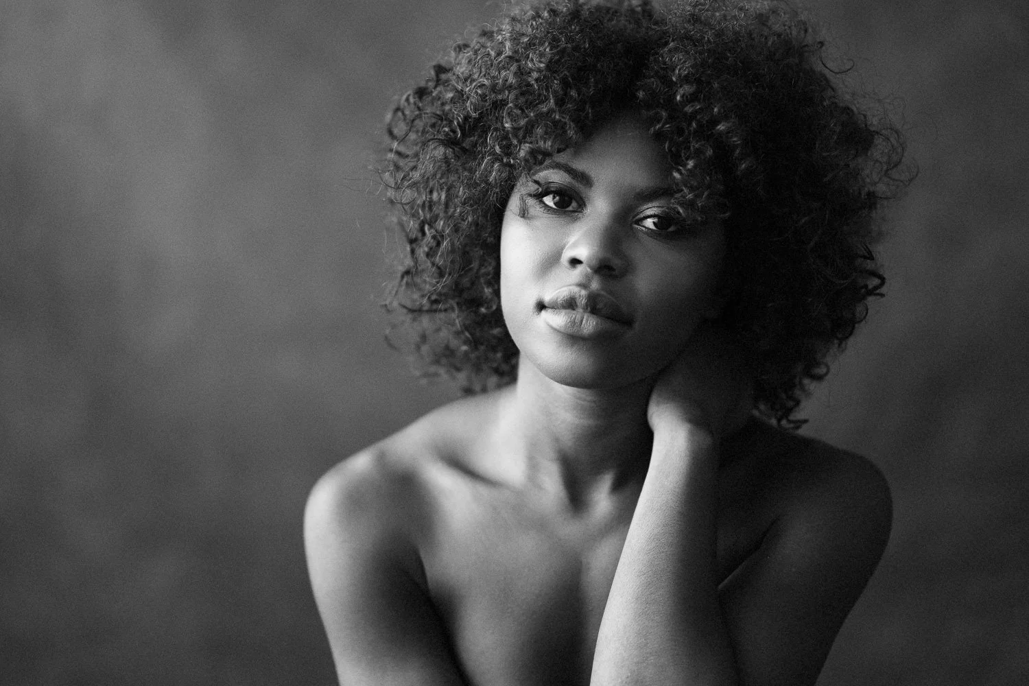 A black and white portrait of a woman with curly hair, looking directly at the camera with a gentle expression.