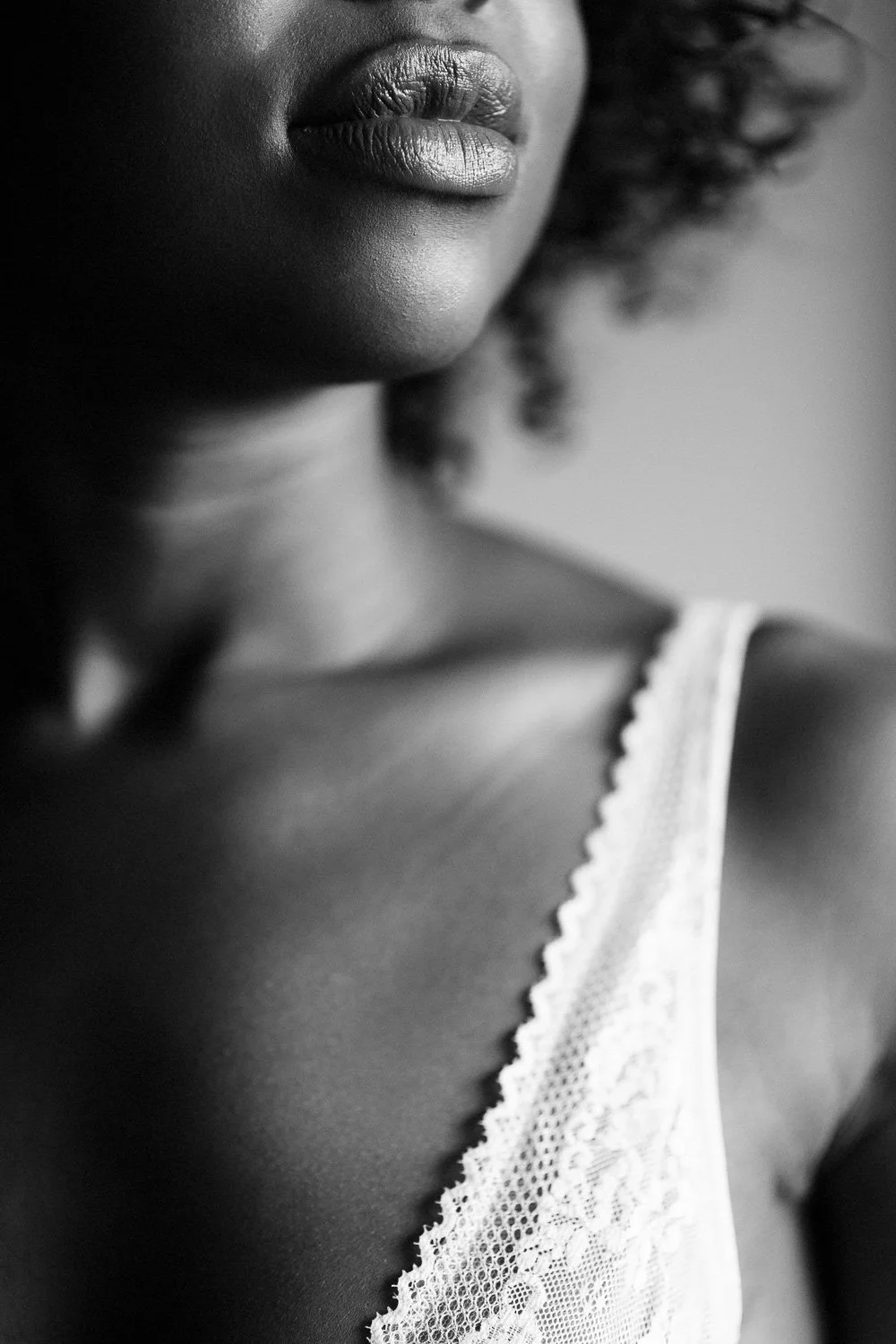 Close-up of a woman's face and shoulder, focusing on her lips and lace top, in black and white.