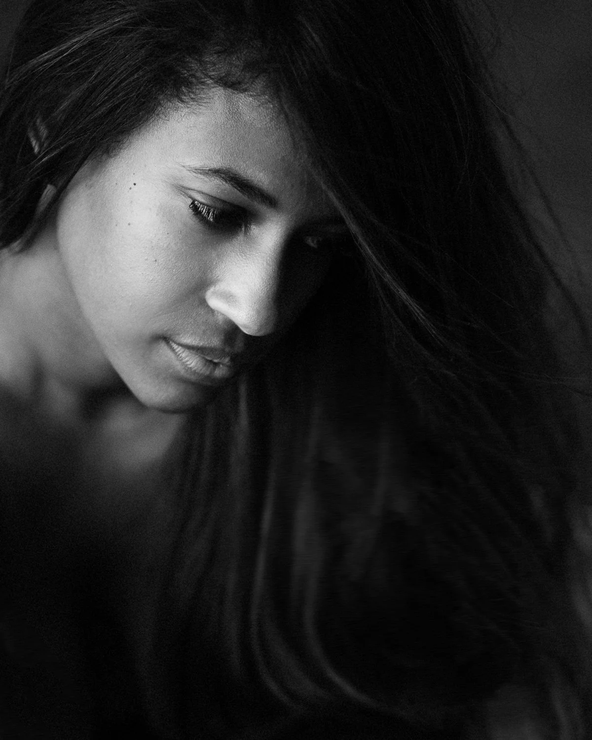 Close-up black and white portrait of a woman with long dark hair, looking downward softly.