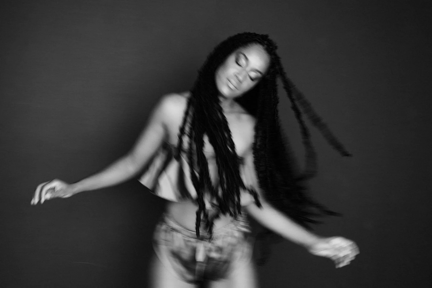 Black and white photograph of a woman with long, braided hair, dancing with her eyes closed and a relaxed expression.