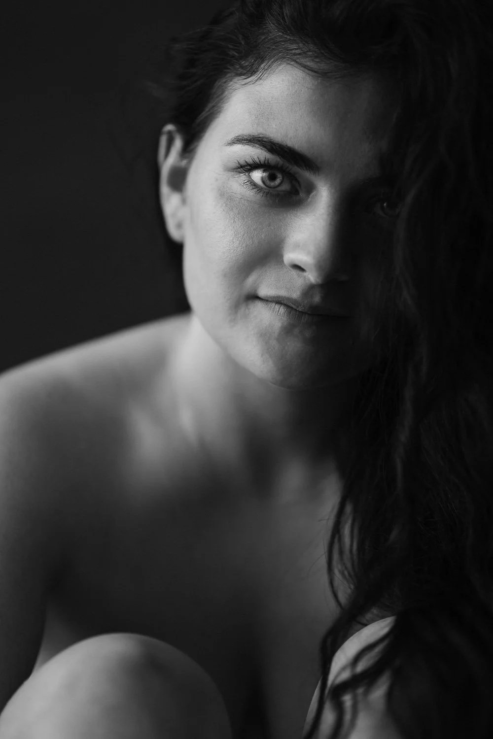 Black and white portrait of a woman with intense eyes, partially covered by dark hair, looking directly at the camera.