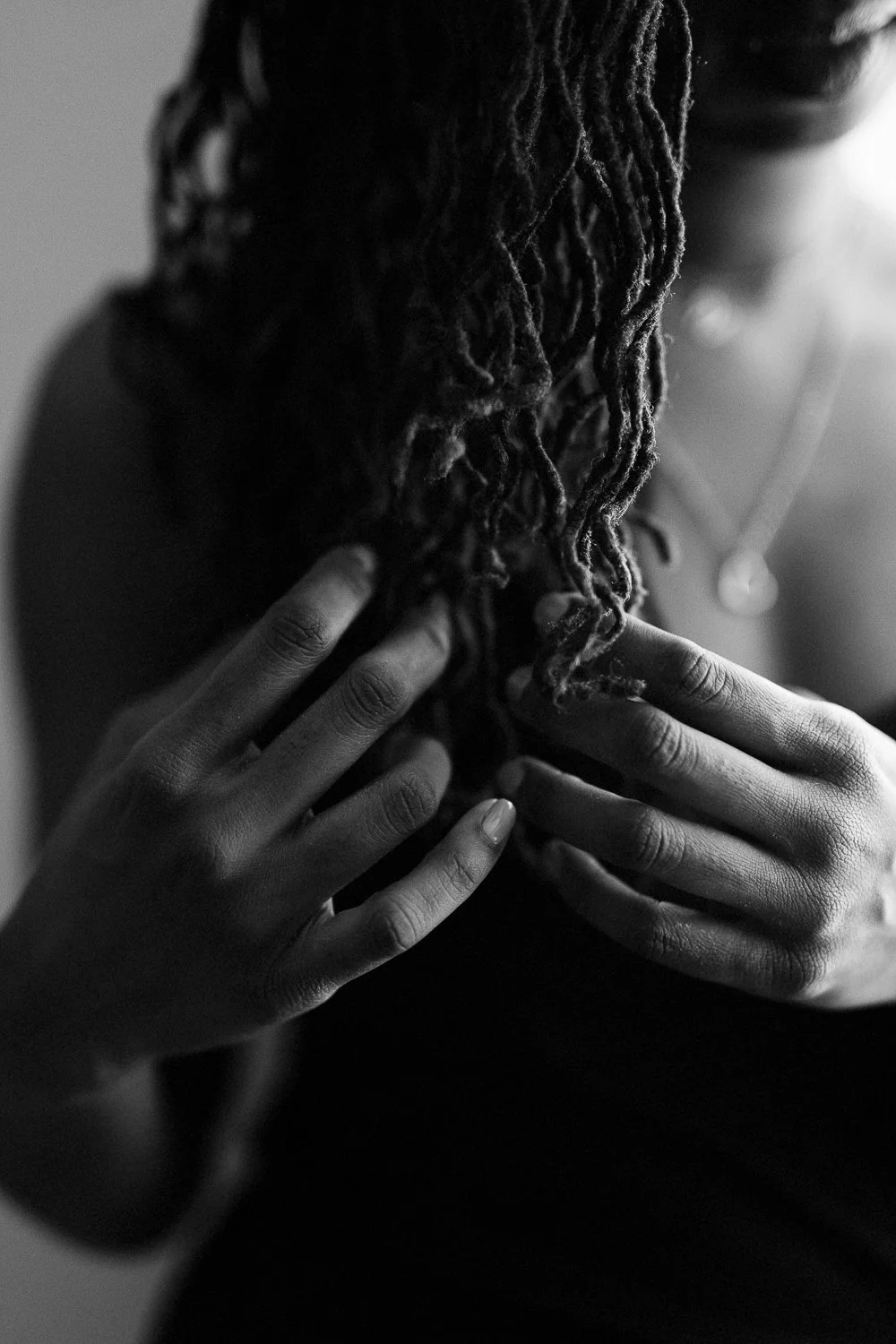 Close-up of a person with dreadlocks, gently touching them with both hands, in black and white.