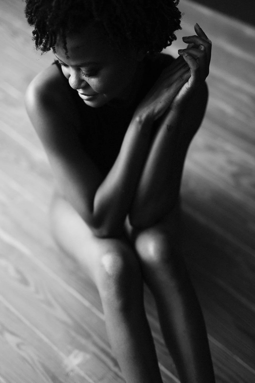 Black and white photo of a woman sitting on the floor with her arms crossed around her knee, looking down with a peaceful expression.