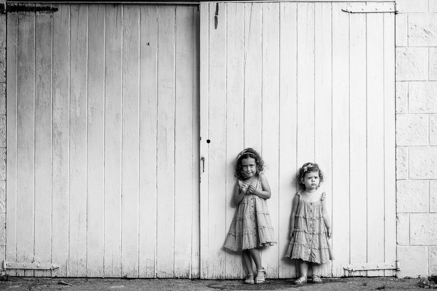 Two young girls in dresses standing against a large wooden door.