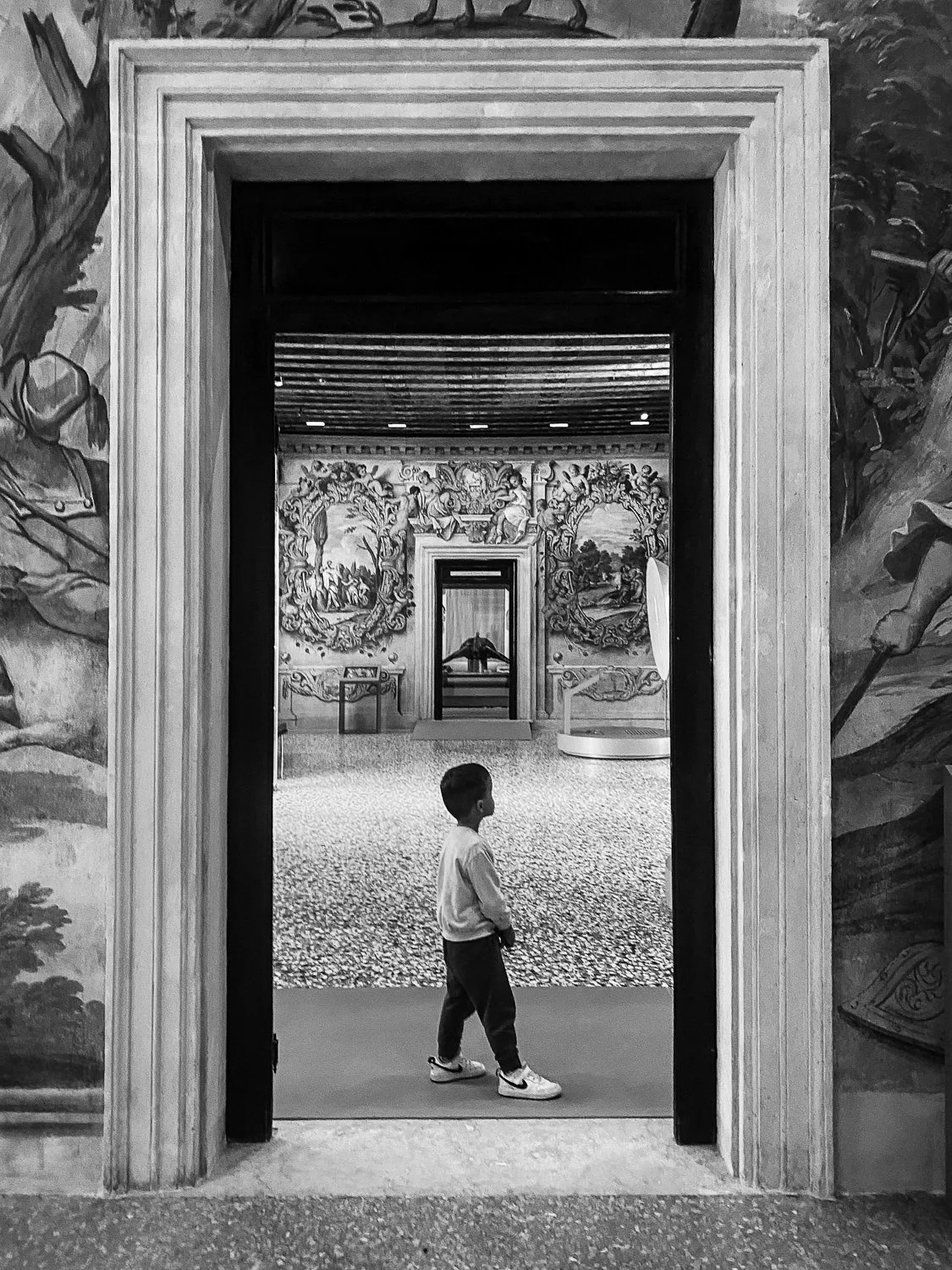 A young boy walking through a doorway into a museum exhibit room with ornate wall decorations and paintings.