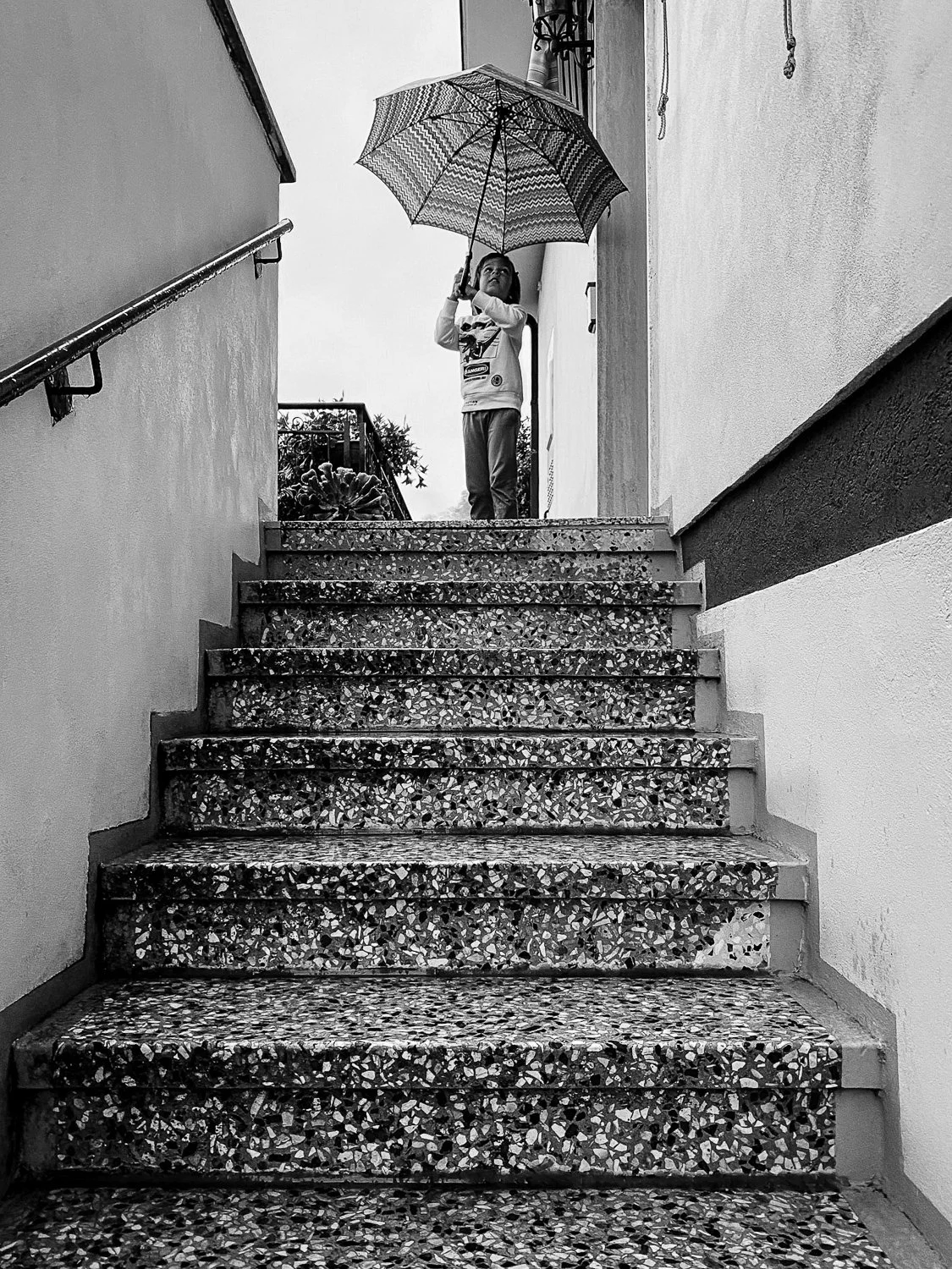 A young child holding an umbrella while standing at the top of a staircase outside a building.