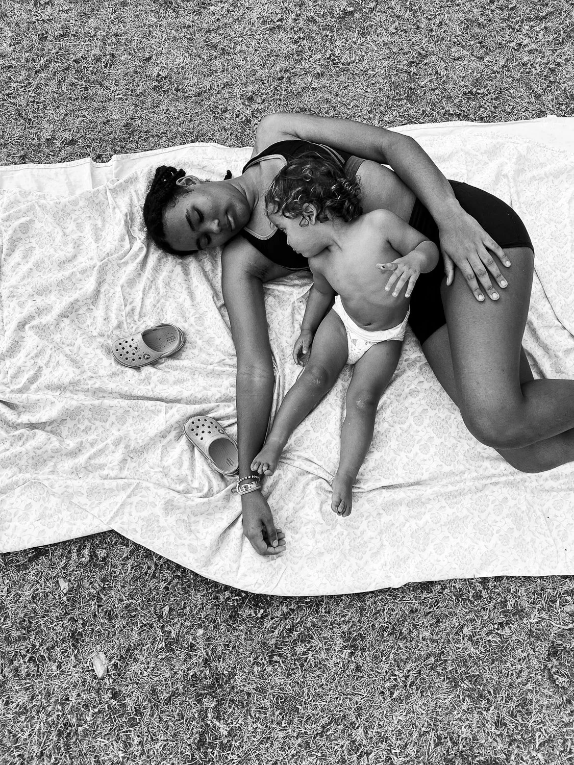 A woman and a young child lying on a blanket in a grassy area, sleeping together.