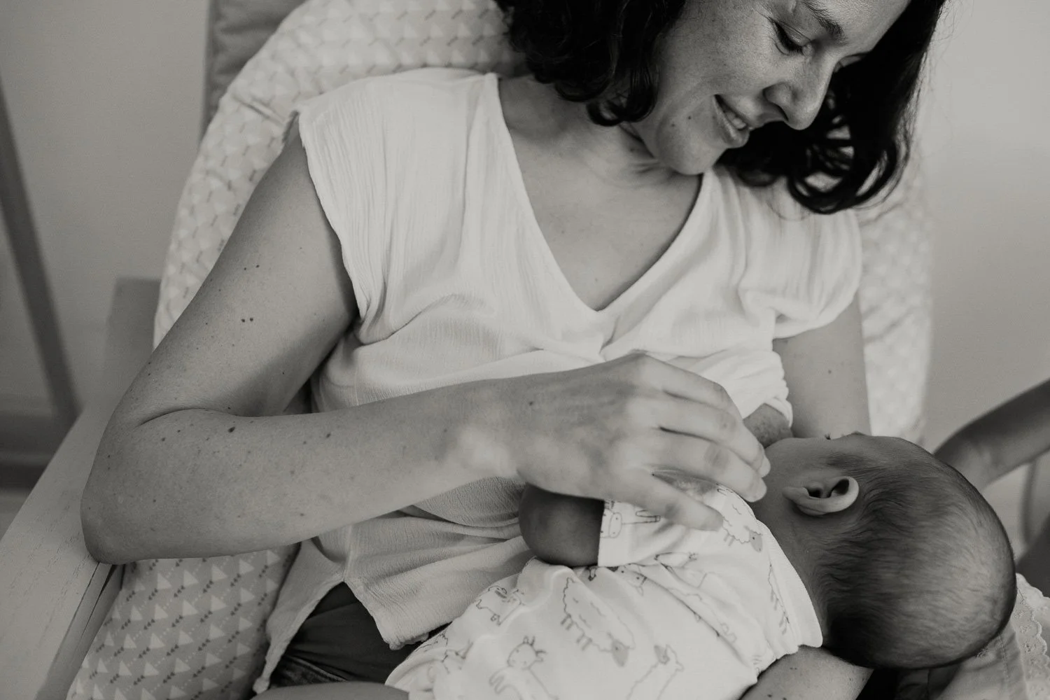 A woman smiling while breastfeeding a baby in a hospital bed.