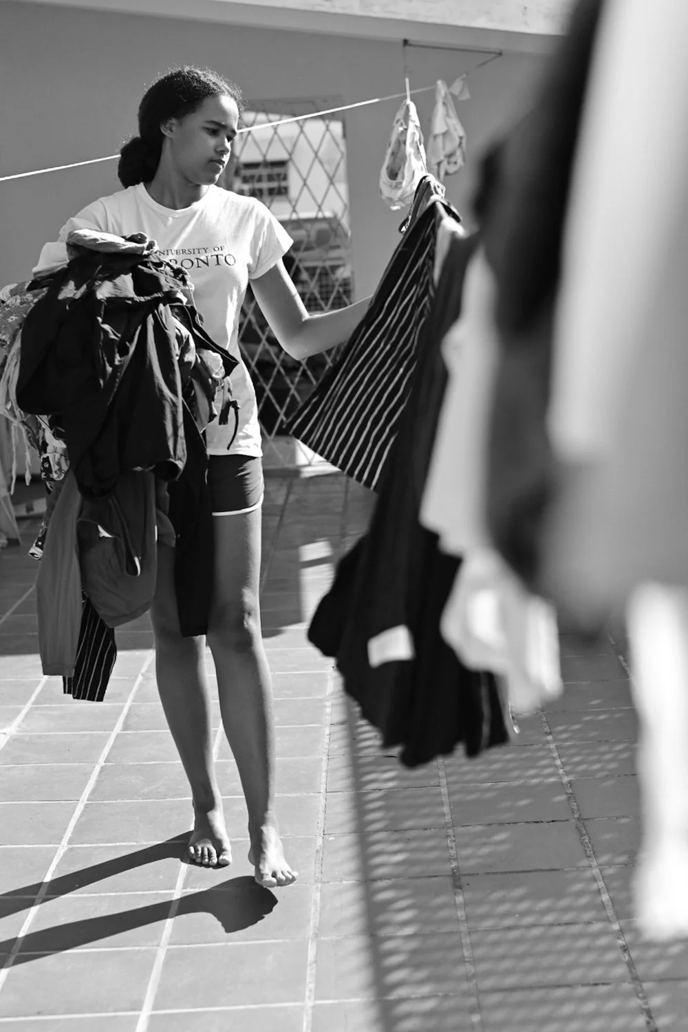 A woman sorting clothes on a clothesline on a rooftop, wearing a University of Toronto t-shirt, holding a pile of laundry.
