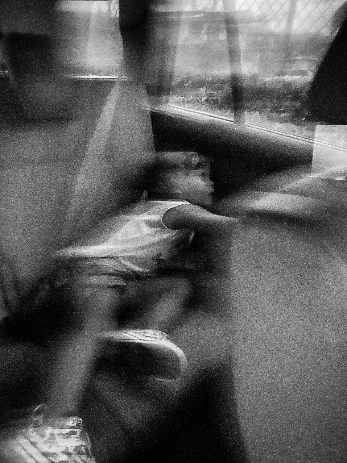 A child is lying down on a bus seat, looking out the window. The photo is in black and white.