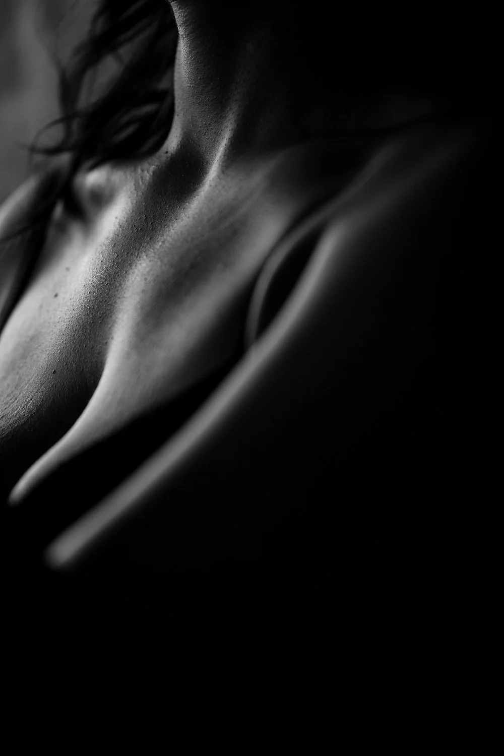 Close-up black and white photograph of a person's shoulder and collarbone, with wet skin and flowing hair.