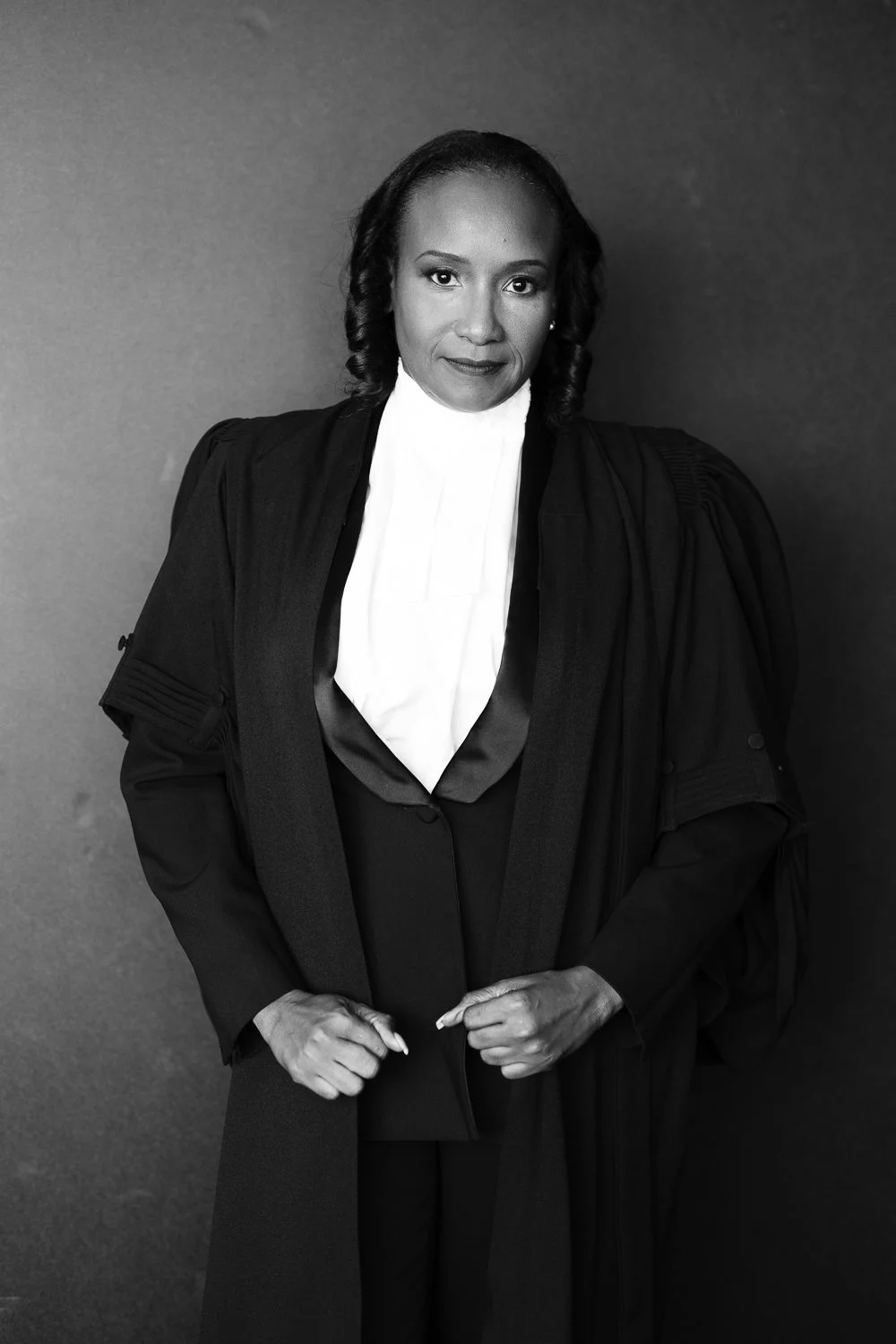 Black and white photograph of a female judge in judicial robes with a white collar, standing against a neutral background.