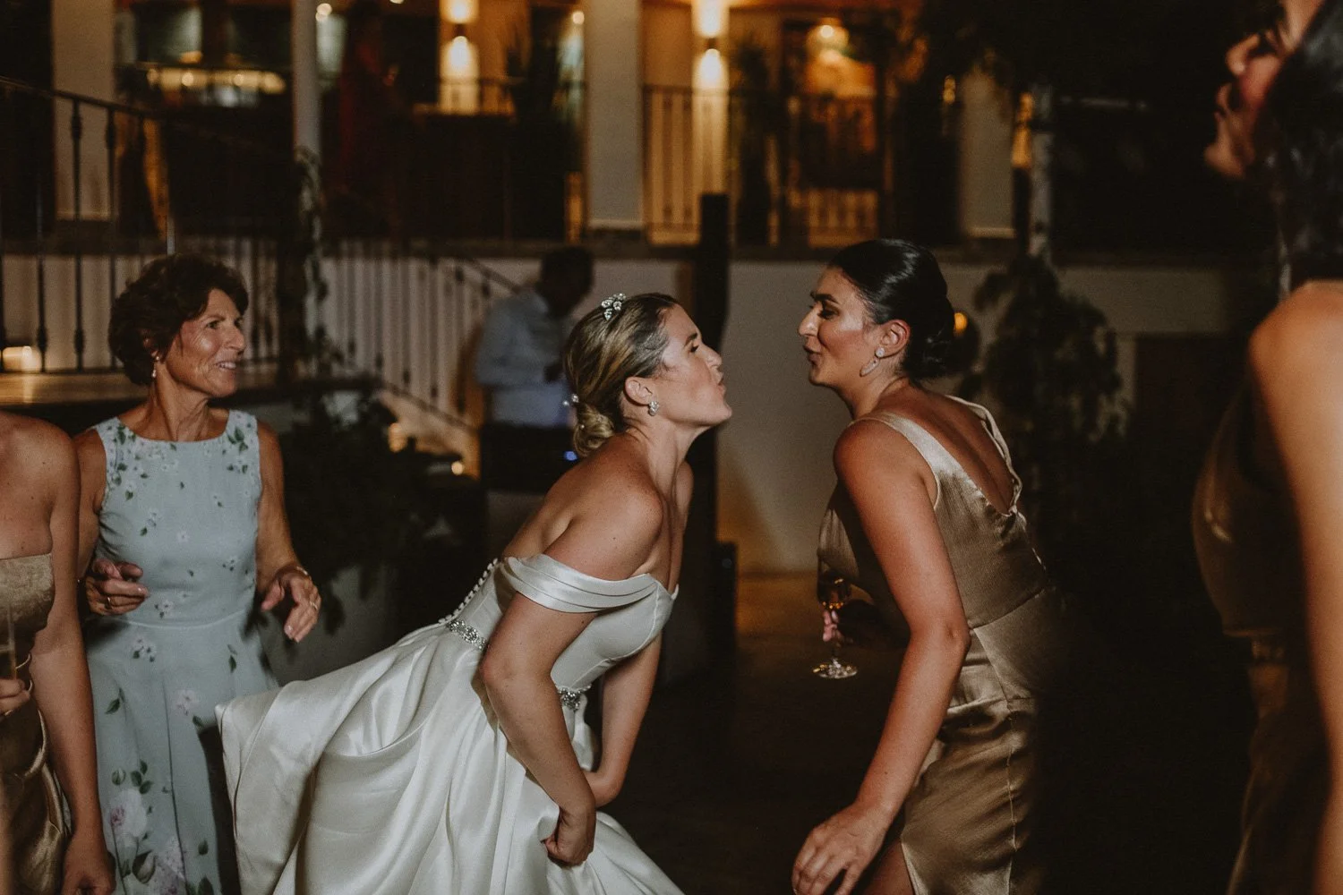 Two women, one in a wedding dress, face-off in a heated moment at a party with other women in the background.