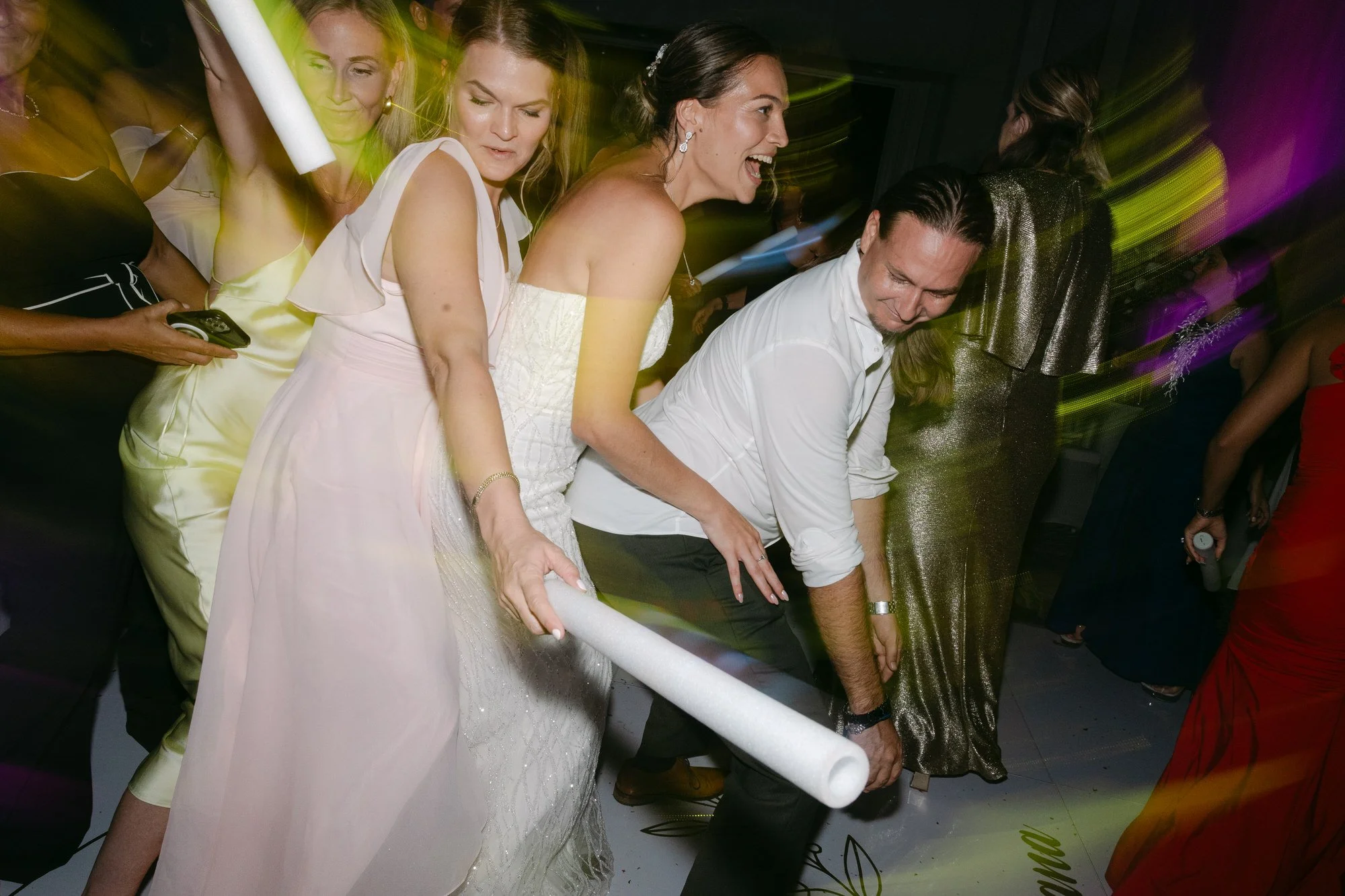People dancing and celebrating at a party, with one woman holding a rolled object and others smiling and enjoying the moment.