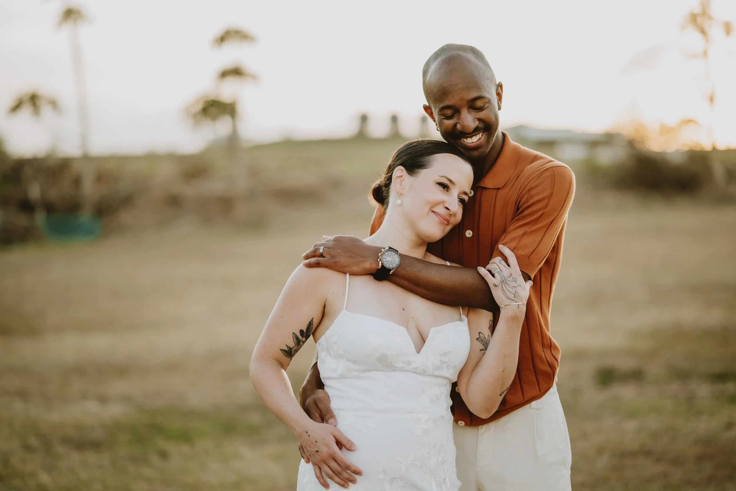 A happy couple embracing outdoors during sunset, with trees in the background.
