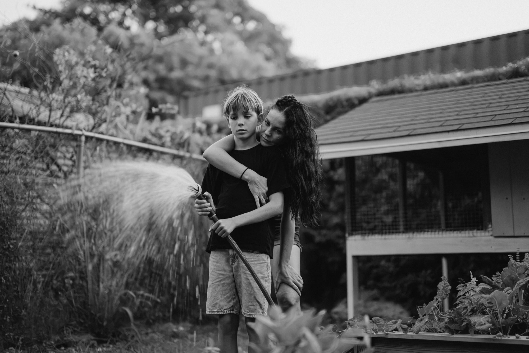 mom hugging her son as he waters the garden
